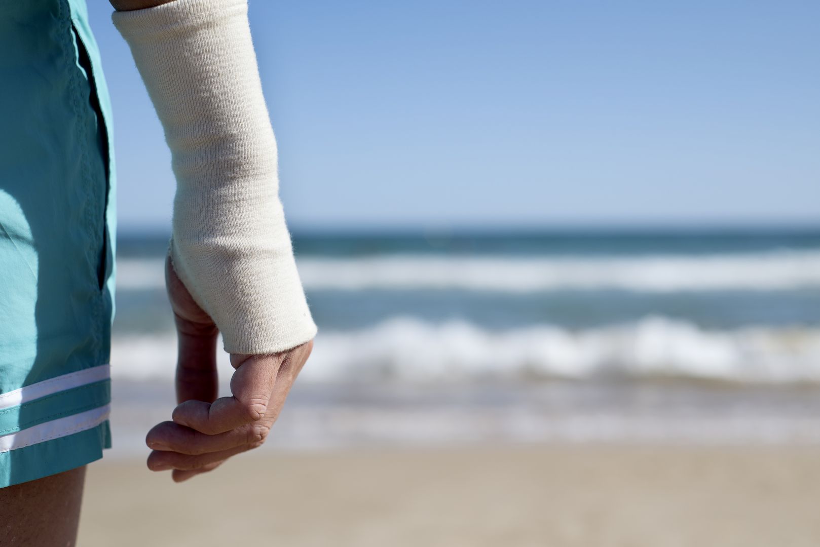 Reiseunfallversicherung Person mit Gipshand am Strand